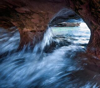 sea cave wave action through a sandstone port hole along the coastline of cat island in the apostle islands