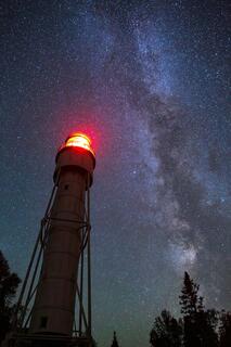 devil's island lighthouse with red light illuminated and the milky way rising over it in dark night skies