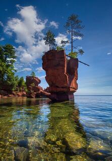 large sea stack with clear water and boulders and a sunny sky on stockton island in the apostle islands