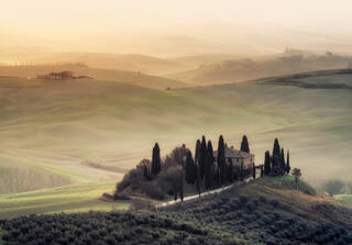 val d'orcia in tuscany italy at sunrise with mist and cypress trees and rolling hills.