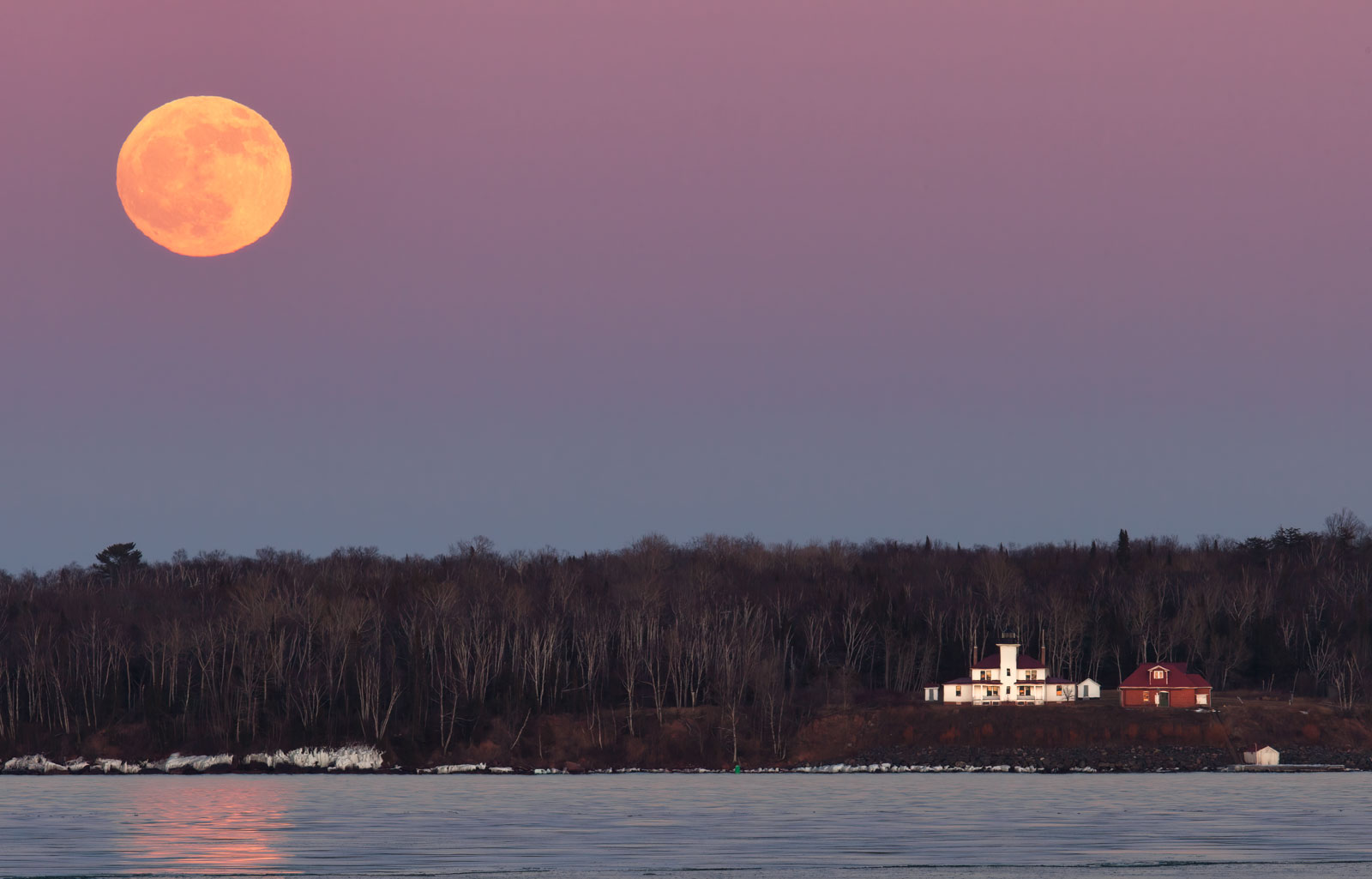 the full moon rises behind the raspberry island lighthouse in the apostle islands on lake superior.