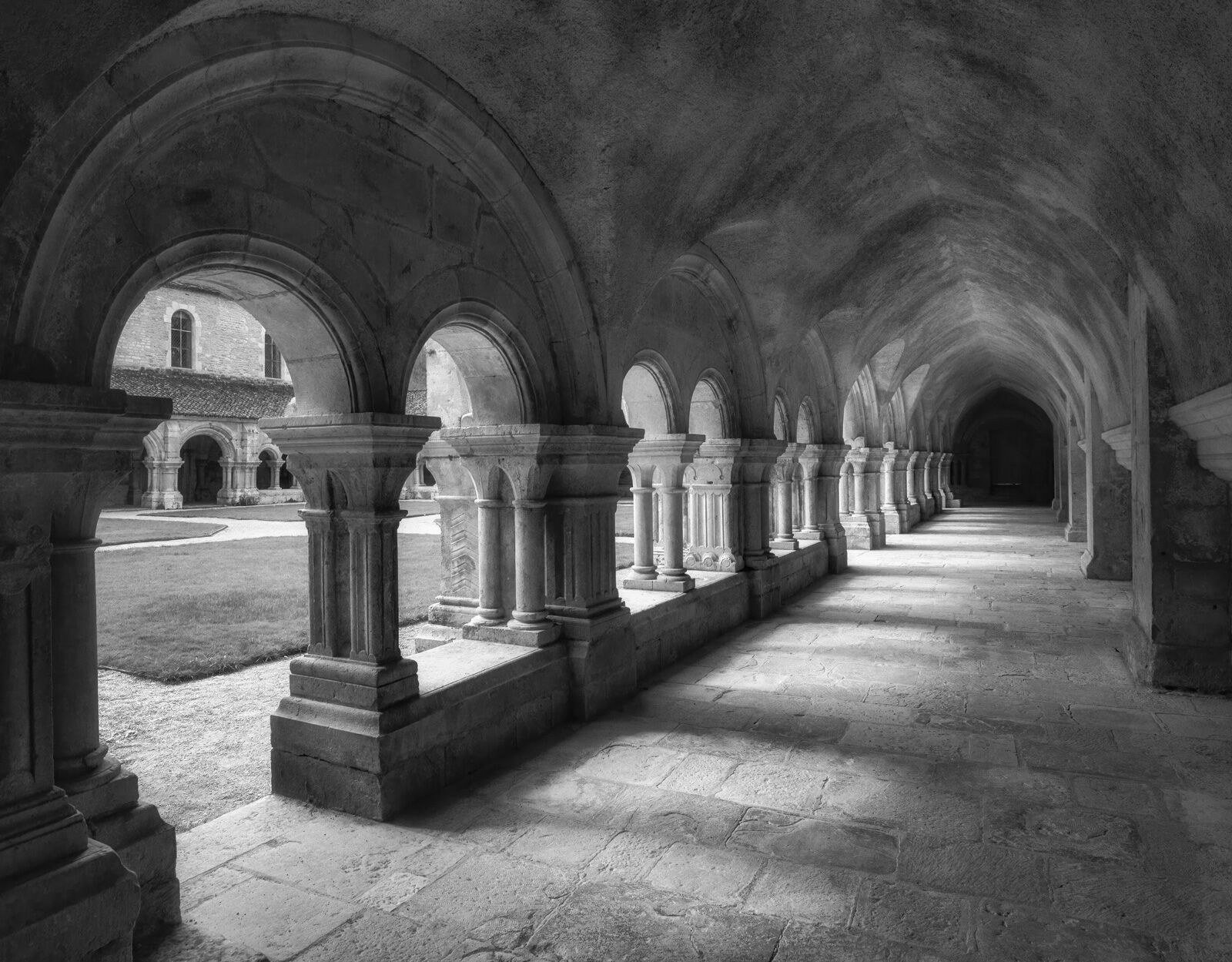 inside the cloister of abbey fontenay with afternoon sunlight beaming through the stone pillars.