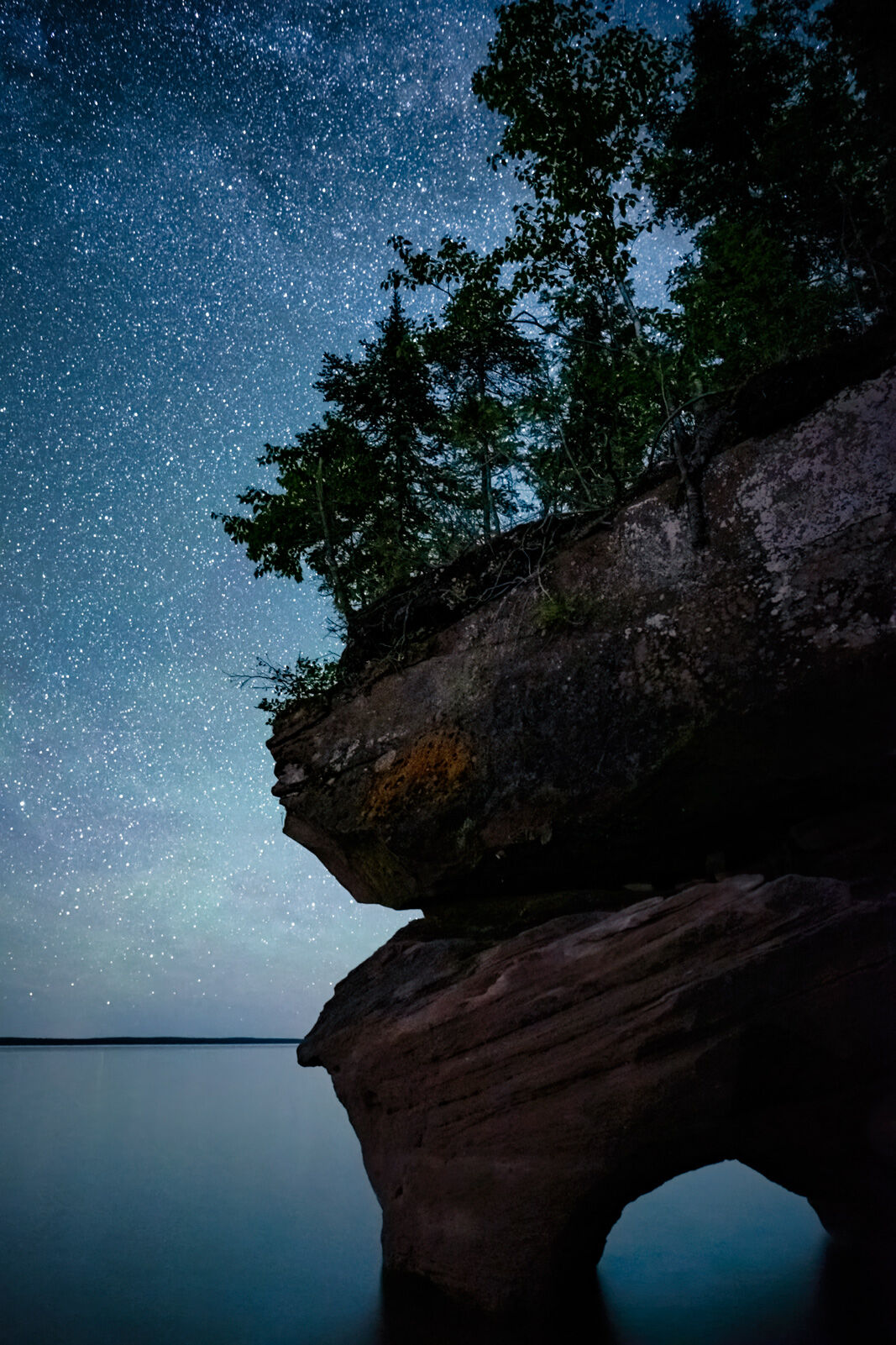 a night time image of a sandstone cliff with a porthole and the starry sky above