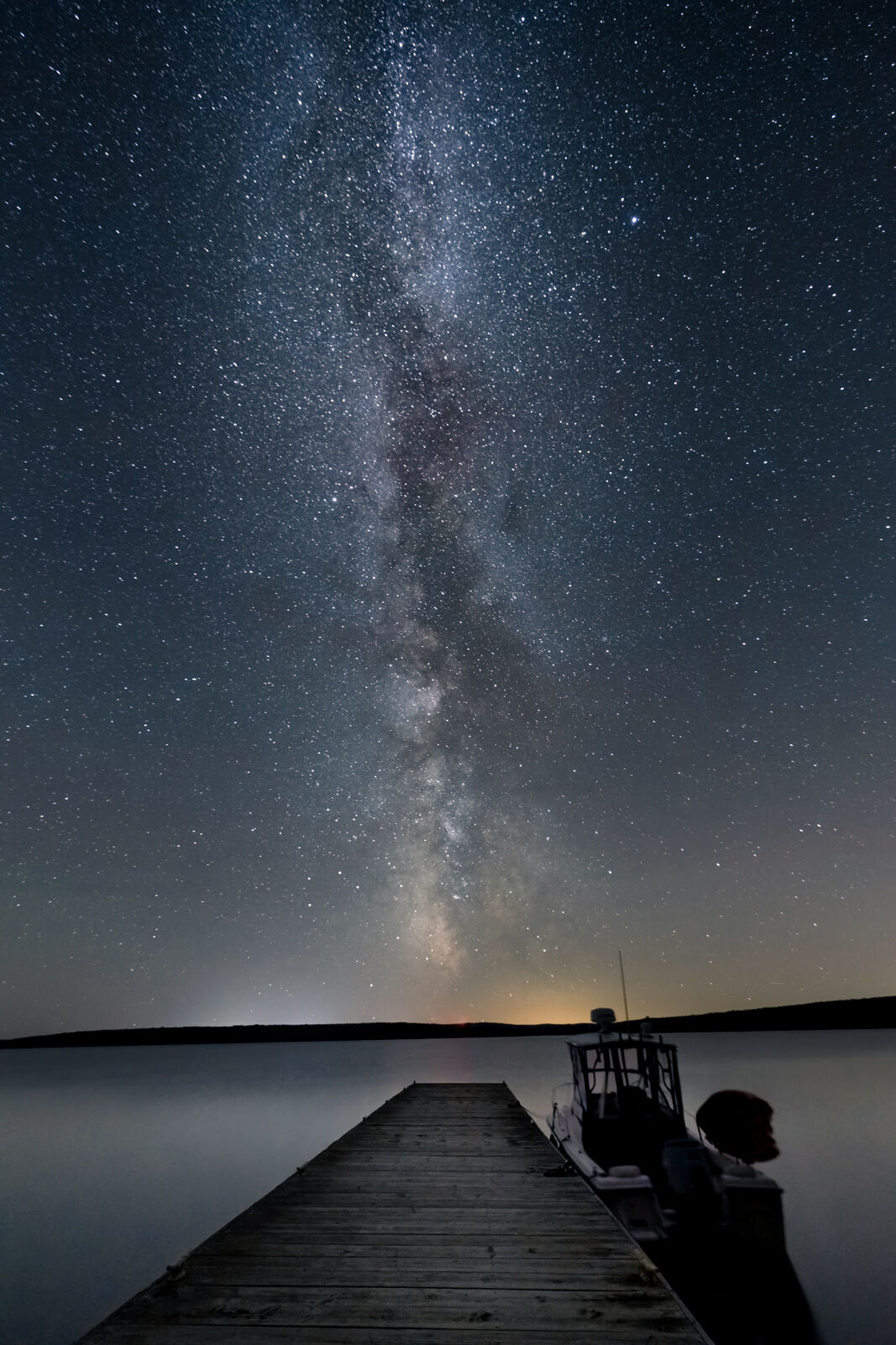 milky way in the night sky with a dock and boat in the foreground